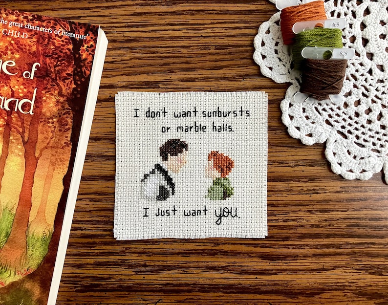 May include: Cross-stitch embroidery with a white background, featuring two figures, a man and a woman, with the text "I don't want sunbursts or marble halls. I just want you."