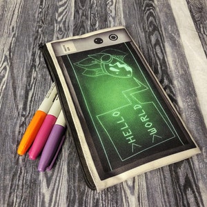 May include: A white canvas pencil case with a black and green design. The design features a cartoon character with a green screen displaying the text "HELLO WORLD".