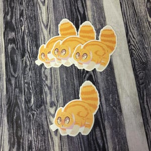 May include: Four orange and white cat stickers with cartoon-style faces. The stickers are on a dark wood background.