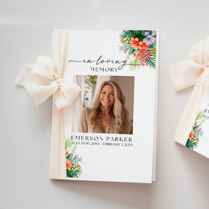 May include: White memorial booklet with a photo of a woman, floral accents, and the text "In Loving Memory." The booklet is tied with a cream-colored ribbon. The name "Emerson Parker" and dates are printed below the photo.
