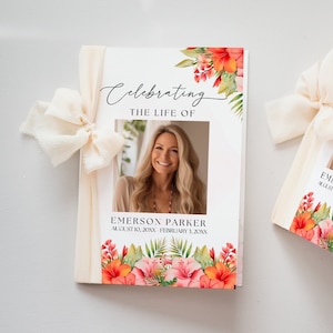 Puede incluir: Dos folletos conmemorativos con una foto de una mujer, detalles florales y el texto "Celebrating The Life Of Emerson Parker". Los folletos están atados con una cinta color crema. El diseño floral incluye flores rojas y rosas.