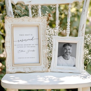 Op de afbeelding: Een witte stoel met een wit frame en een bord met de tekst "Deze stoel is gereserveerd ter nagedachtenis aan de vader van de bruid, Ethan Jacobs, voor altijd in onze harten". Een ingelijste foto van een man staat op de stoel.