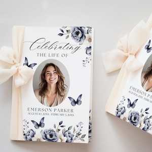 Puede incluir: Dos libretos conmemorativos con una cinta color crema. La portada presenta una foto, el texto "Celebrando la vida de" y el nombre "Emerson Parker". Diseños florales y de mariposas en azul y blanco decoran la portada.