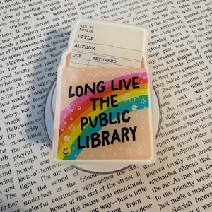 May include: A rectangular acrylic pin featuring a vintage library checkout card at the top with the text 619.37 RS71.n, TITLE, AUTHOR, DUE, and RETURNED. Below is a rainbow graphic with the black text LONG LIVE THE PUBLIC LIBRARY.