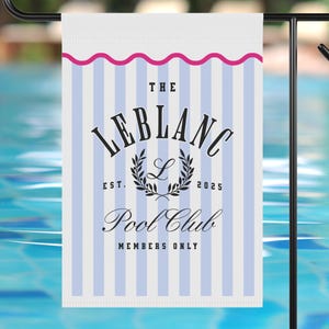 May include: A rectangular garden flag with a blue and white striped design. The flag displays the text "THE LEBLANC POOL CLUB MEMBERS ONLY" in a decorative font. A pink wavy line borders the top. The flag is on a black metal stand, near a swimming pool.