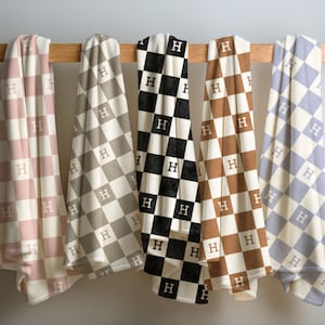 Può includere: Cinque coperte a quadri con la lettera "H" al centro di ogni quadrato. Le coperte sono rosa, marrone, nero e bianco e blu chiaro.