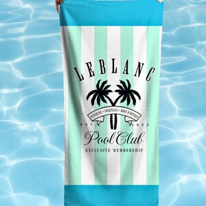 May include: A rectangular beach towel featuring vertical mint green and white stripes with solid bright blue top and bottom borders. The center displays a black graphic of two palm trees, the text LEBLANC, Pool Club, and EXCLUSIVE MEMBERSHIP.