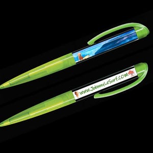 Op de afbeelding: Twee groene pennen met zwarte inkt. Eén pen heeft een blauwe en witte afbeelding van een surfer op een golf. De andere pen heeft de tekst "www.JohnnyLeSurf.com" erop gedrukt.
