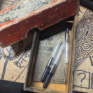 May include: A vintage wooden box, open to reveal pen nibs and ink cartridges. The box has a distressed red and white exterior. The text "Tekpar products are manufactured by James Neil (Sheffield) Limited" is printed on the box.