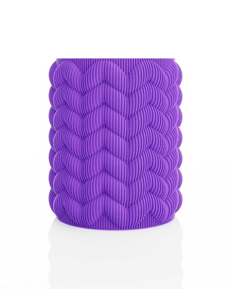 May include: A cylindrical, purple container with a textured, wave-like pattern. The design features vertical ridges that create a repeating chevron motif around the entire body of the container. The object is set against a white background.