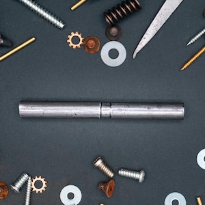 May include: A collection of metal engineering components, such as screws, washers, springs, and gears, displayed on a dark background. A central metal rod is bisected. A dial gauge and a metal ruler are also present, suggesting a mechanical theme.