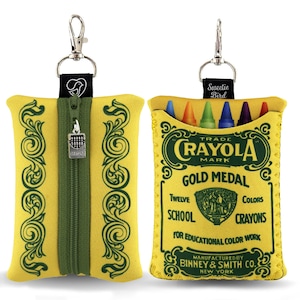 May include: Yellow crayon case with a green zipper and decorative scrollwork. The case has a silver clip and a tag that says "Sweetie Bird". The case is designed to look like a Crayola crayon box and holds twelve crayons.