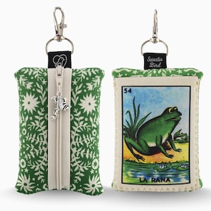 May include: Two small, rectangular pouches with silver-tone hardware. One pouch is green with a white floral pattern and a silver frog zipper pull. The other pouch features a vintage-style image of a green frog with the text "LA RANA". The text "Sweetie Bird" is on a black tag.