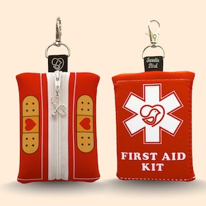 Pode incluir: Duas bolsas vermelhas de primeiros socorros com ferragens prateadas. Uma bolsa tem zíper e gráficos de band-aid. A outra bolsa tem um símbolo branco da estrela da vida e as palavras "FIRST AID KIT". Ambas as bolsas têm o logotipo "Sweetie Bird".