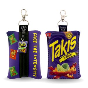 Könnte beinhalten: Zwei lila Stoffbeutel mit silbernen Schlüsselanhängern. Ein Beutel zeigt den Text "FACE THE INTENSITY" und kleine Takis-Taschengrafiken. Der andere Beutel zeigt das Takis Fuego-Logo mit einer Limette und Flammen.