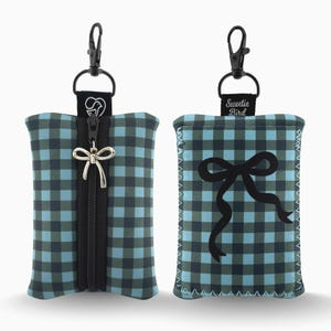 Op de afbeelding: Een blauw-groen geruit etui met een zwarte rits en een zilveren strikbedel. De etui heeft een zwarte clip en een zwarte band met een hart- en hondenontwerp. De andere kant heeft een zwart strikdesign en de tekst "Sweetie Bird".