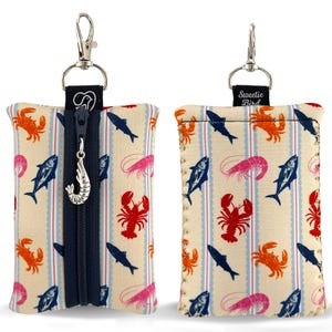 May include: Two rectangular pouches with a cream background featuring a repeating pattern of red lobsters, orange crabs, pink shrimp, and dark blue fish. The left pouch has a dark blue vertical zipper with a silver shrimp charm and a metal clip.
