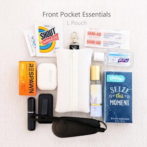 May include: An assortment of everyday carry items, including a white zippered pouch, mints, earbuds, hand sanitizer, tissues, and a small perfume bottle. The image also includes a black eye mask and a Shout Wipe & Go packet.