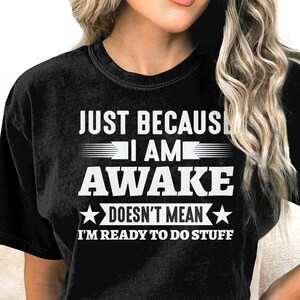 May include: Black t-shirt with white text that reads "Just because I am awake doesn't mean I'm ready to do stuff".