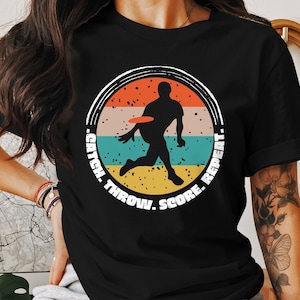 May include: Black t-shirt with a retro-style graphic of a person playing frisbee. The graphic includes the text "Catch. Throw. Score. Repeat."