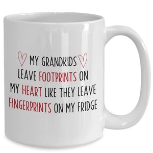 Peut inclure: Une tasse à café en céramique blanche avec un motif noir et rouge. Le texte dit "♡MY GRANDKIDS LEAVE FOOTPRINTS ON MY HEART LIKE THEY LEAVE FINGERPRINTS ON MY FRIDGE".