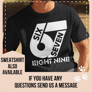 May include: Black t-shirt with a large white graphic featuring the numbers "67" and the words "SIX" and "SEVEN". The text "EIGHT NINE" is below the numbers. Additional text reads "SWEATSHIRT ALSO AVAILABLE".