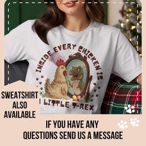 以下が含まれることがあります： ユーモラスなグラフィックがプリントされた白いTシャツ。デザインは、鏡を見てT-Rexを見ている鶏が特徴です。テキストは「INSIDE EVERY CHICKEN IS A LITTLE T-REX」と書かれています。「SWEATSHIRT ALSO AVAILABLE」の文字もプリントされています。