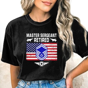 May include: Black t-shirt with a distressed American flag design and the text "Master Sergeant Retired". The flag features a blue Air Force insignia.