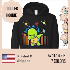 May include: Black toddler hoodie with a green turtle dabbing and the text "Shell We Dab" in rainbow colors. The turtle is surrounded by colorful paint splatters.