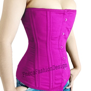 May include: A fuchsia pink corset with a busk closure and a satin ribbon detail. The corset is made of a sturdy cotton fabric and has a smooth, matte finish. The corset is worn by a person with blue jeans.