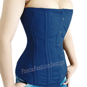 Può includere: Un corpetto in cotone blu scuro con chiusura a busc e una fila di bottoni sul davanti. Il corpetto è indossato sopra un paio di jeans blu con un design grafico.