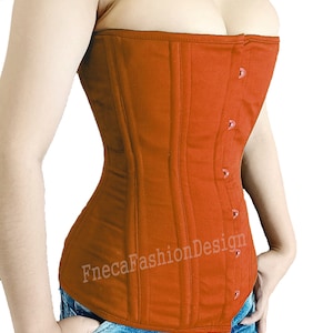 May include: A rust-colored, strapless corset with a busk closure and a satin-like finish. The corset has a smooth, quilted texture and is made of a sturdy fabric. The corset is worn over a pair of blue jeans with a graphic design.