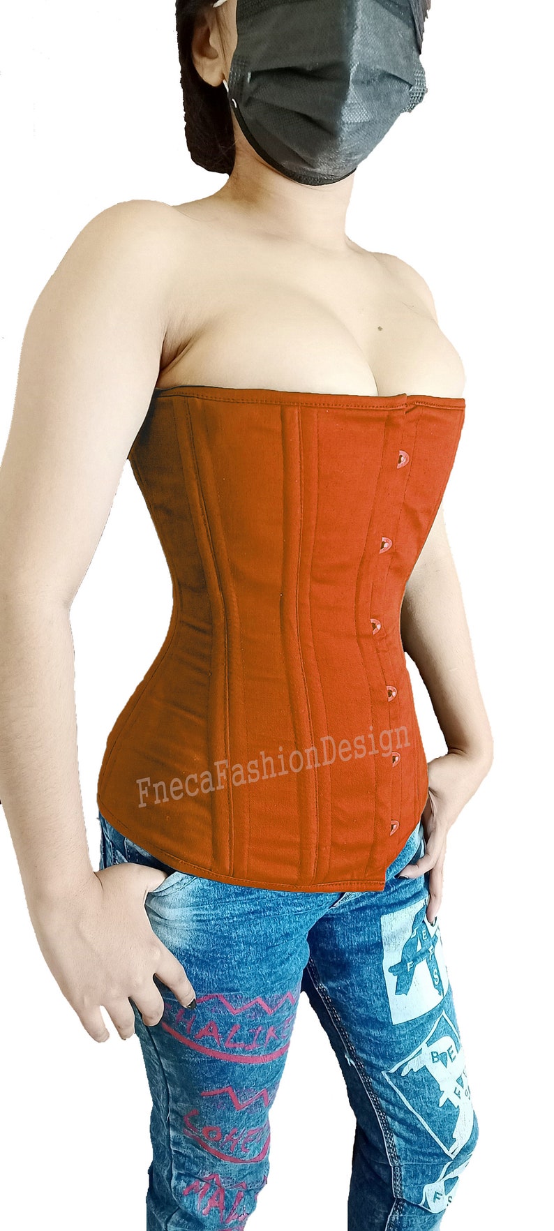 May include: A rust-colored, strapless corset with a busk closure and a satin-like finish. The corset has a smooth, quilted texture and is made of a sturdy fabric. The corset is worn over a pair of blue jeans with a graphic design.