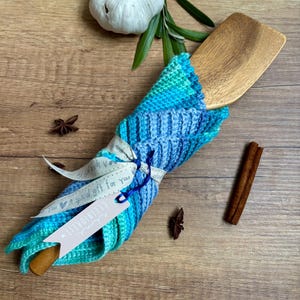 Könnte beinhalten: Ein Holzspatel, umwickelt mit einer blau-türkisfarbenen Strickhülle, gebunden mit einem Band mit der Aufschrift "A special gift for You". Der Spatel liegt auf einer Holzoberfläche mit Knoblauch, Sternanis und Zimtstange.
