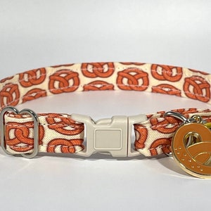 May include: A white and orange cat collar with a pretzel pattern and a gold pretzel charm.