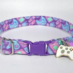May include: Purple and blue cat collar with a white and green video game controller charm. The collar is made of fabric and has a purple plastic buckle.