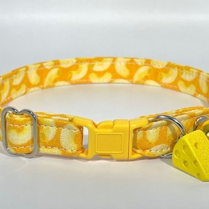May include: A yellow cat collar with a cheese print pattern, a yellow plastic buckle, and a silver bell with a yellow cheese charm.