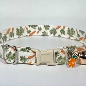 Peut inclure: Un collier de chat blanc avec un imprimé de carottes vertes et orange. Le collier a une boucle argentée et une petite cloche avec un charme de carotte.