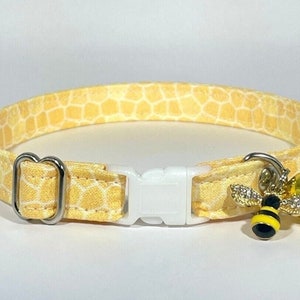 May include: A yellow cat collar with a honeycomb pattern and a bee charm with a bell. The collar has a white plastic buckle and a silver metal D-ring.