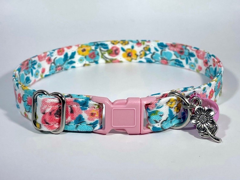 Puede incluir: Un collar para gato con estampado floral blanco, azul y rosa con una hebilla de pl&aacute;stico rosa y un dije plateado con dise&ntilde;o de flor.