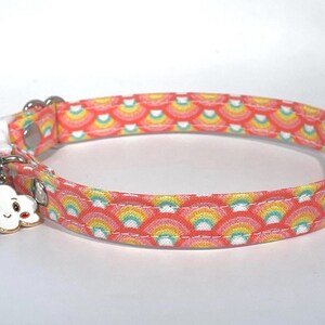 Puede incluir: Un collar para gato rosa y amarillo con un patr&oacute;n de arco&iacute;ris y un peque&ntilde;o amuleto de nube con una cara sonriente.