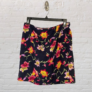 May include: A dark blue skirt with a floral print featuring pink, yellow, and white flowers. The skirt has a wrap-around style and a slightly flared silhouette.