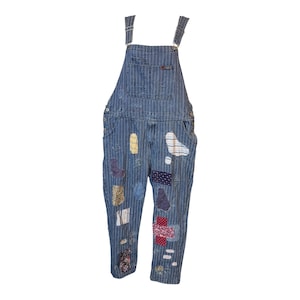 May include: Blue and white pinstriped denim overalls featuring a bib pocket and multiple colorful fabric patches sewn onto the legs. The patches include various patterns such as floral, polka dot, and solid colors, creating a textured appearance.