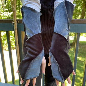 May include: A pair of fingerless arm warmers featuring a color-blocked design of dark charcoal gray and light blue fabric panels. The sleeves have exposed seams and a diagonal construction that extends from the wrist up to the mid-forearm area.