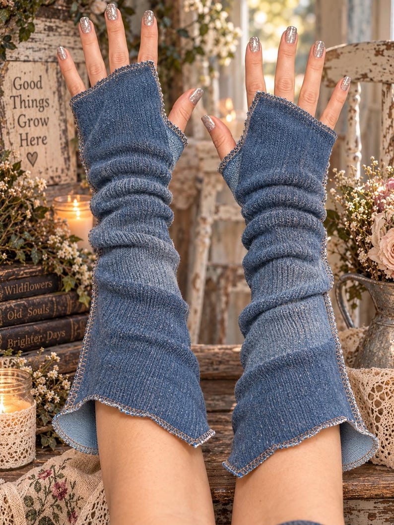 May include: A pair of blue denim fingerless arm warmers featuring a ribbed texture and exposed serged seams along the edges. These long, pull-on sleeves extend from the knuckles to the mid-forearm, showcasing a classic medium-wash blue fabric.