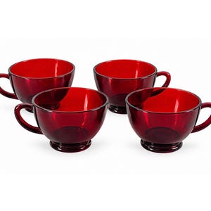 Könnte beinhalten: Ein Set aus vier passenden rubinroten Glastassen, die jeweils eine breite, abgerundete Schalenform, einen stabilen runden Sockel und einen geschwungenen Seitengriff aufweisen. Das durchscheinende Glasmaterial lässt Licht hindurch.