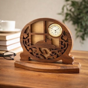 May include: A wooden cat-themed clock with a round, gold-colored clock face. The clock is carved with a cat silhouette and floral designs. The clock sits on a wooden base and is displayed on a wooden table.