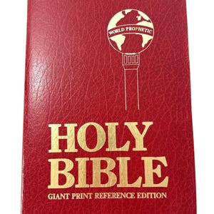 Könnte beinhalten: Eine rote Bibel mit strukturierter Oberfläche und goldener Schrift. Der Einband zeigt eine Grafik eines Globus auf einem Sockel mit dem Text "WORLD PROPHETIC" im Inneren sowie die Worte "HOLY BIBLE" und "GIANT PRINT REFERENCE EDITION" darunter.