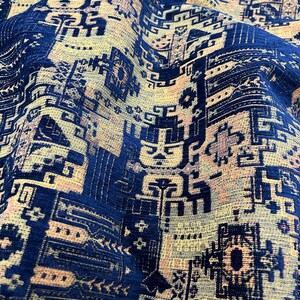 May include: Close-up of a blue and beige patterned fabric with a geometric design. The fabric has a textured surface and a slightly faded appearance.
