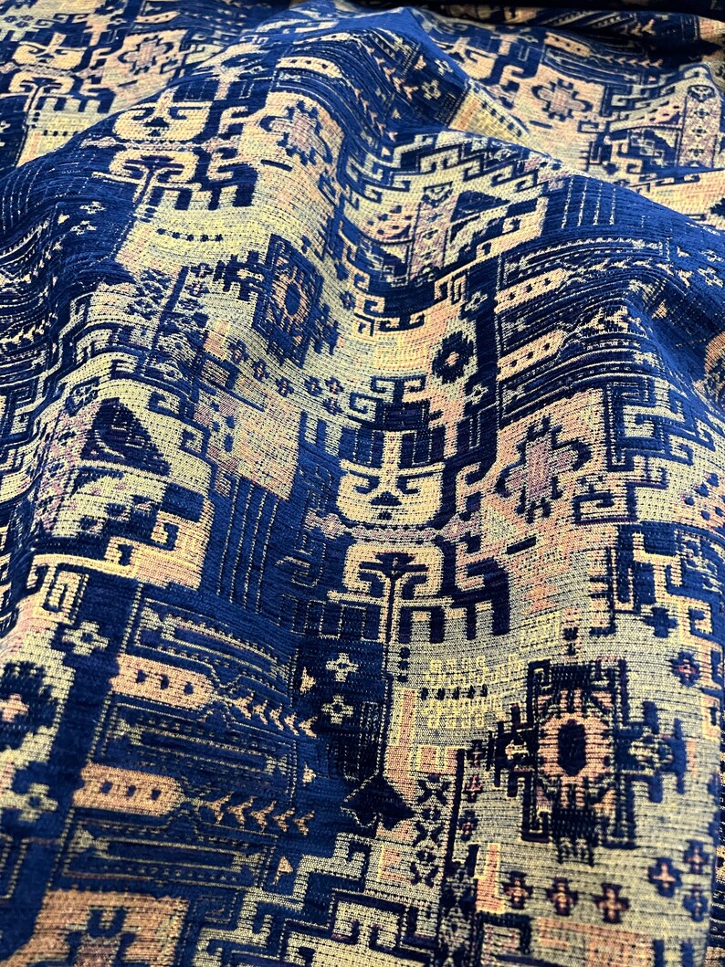 May include: Close-up of a blue and beige patterned fabric with a geometric design. The fabric has a textured surface and a slightly faded appearance.